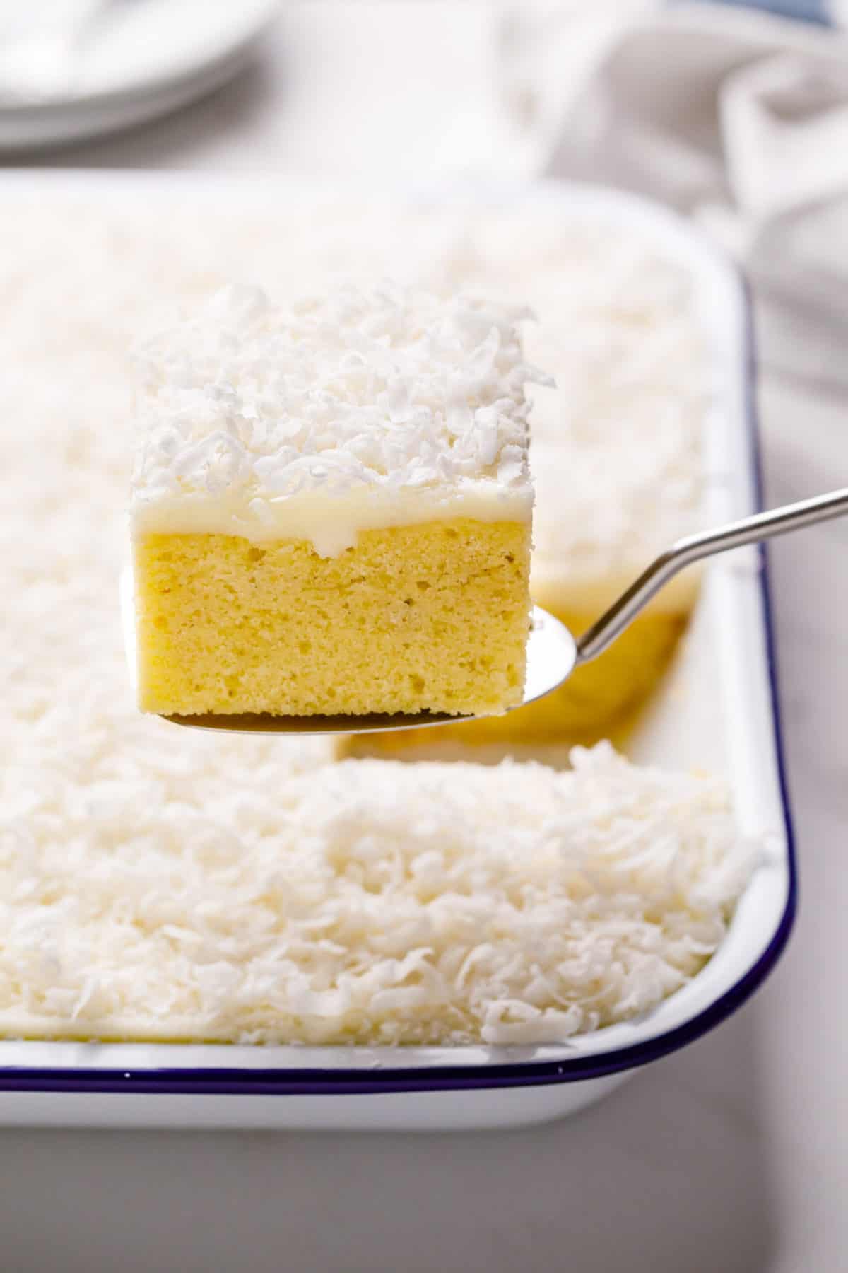 square slice serving of coconut cake with coconut cream frosting sitting on a metal spatula
