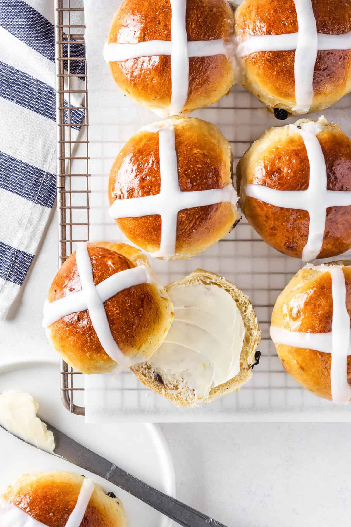 hot cross buns on a wire rack with one bun cut length wise smothered with frosting