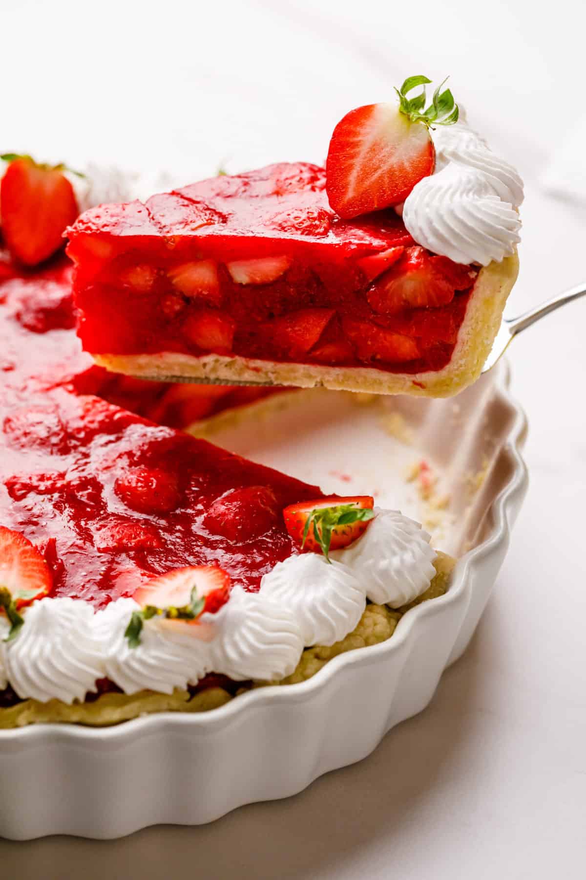 strawberry pie in a pie dish topped with fresh strawberries and chantilly cream