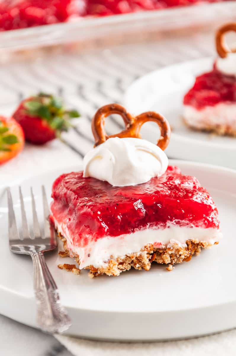 square serving of strawberry pretzel dessert topped with whipped cream and a pretzel
