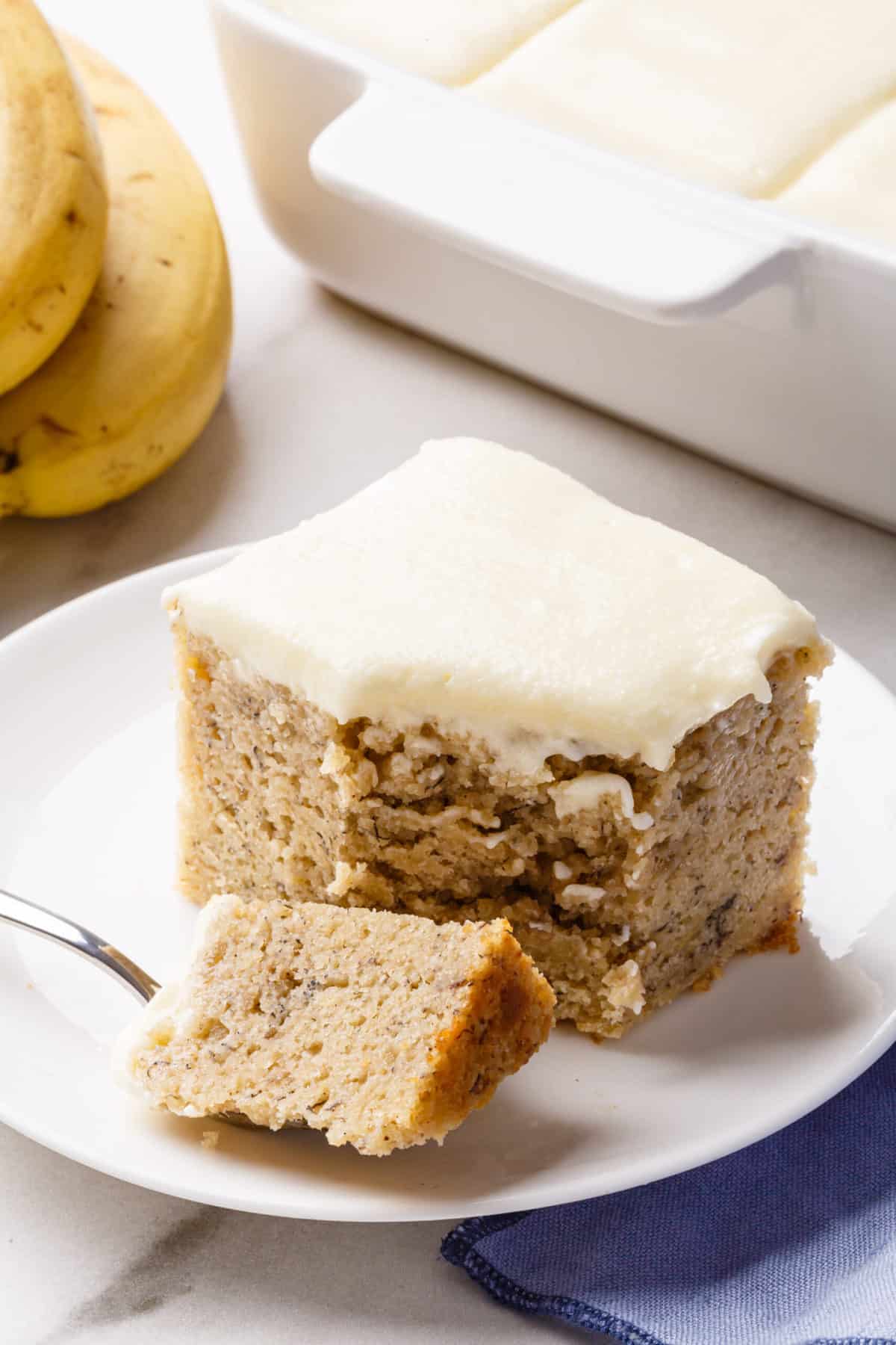 serving of banana cake with cream cheese frosting served on a white plate
