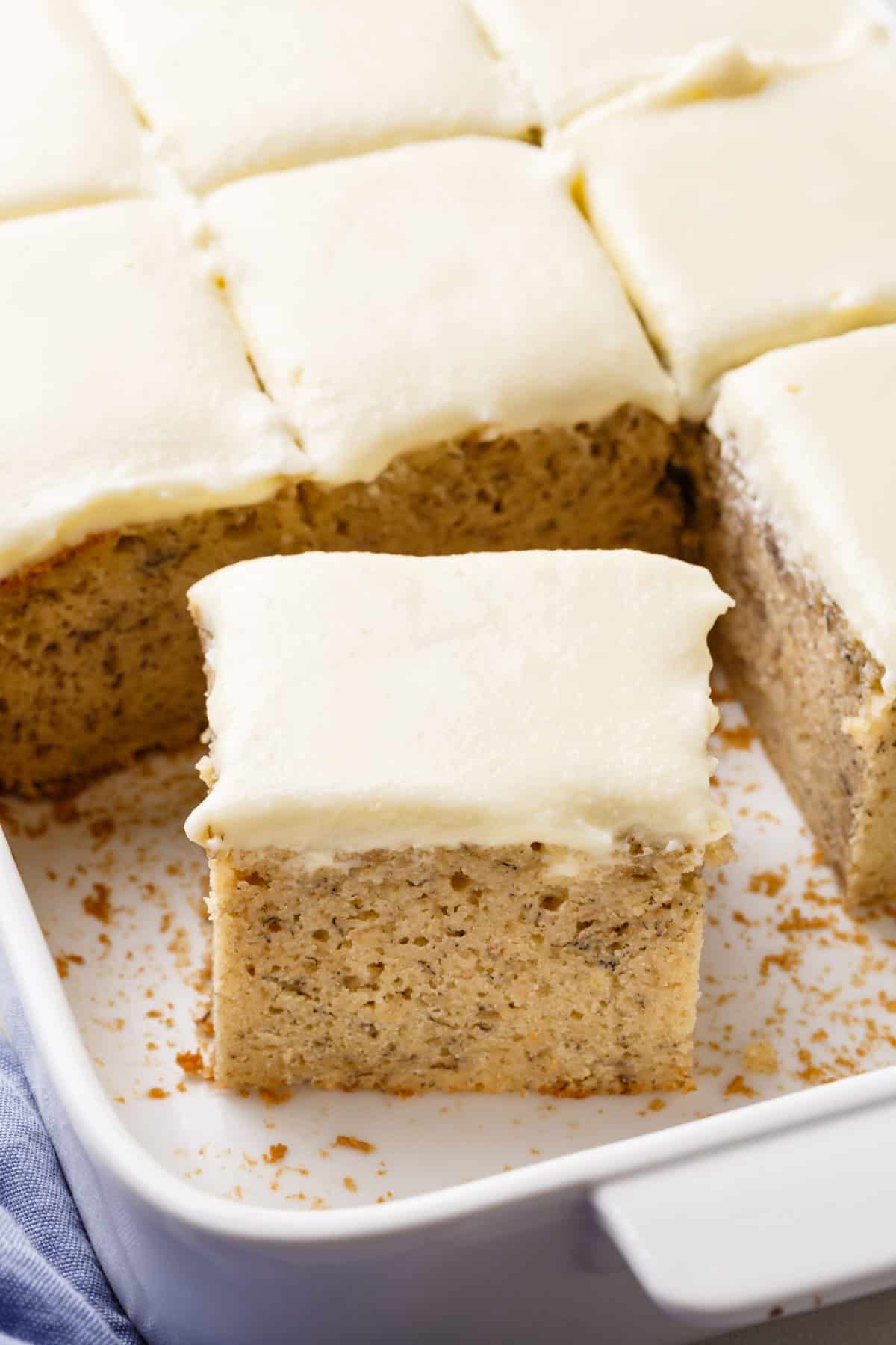 square slice of banana cake with cream cheese frosting in a baking dish