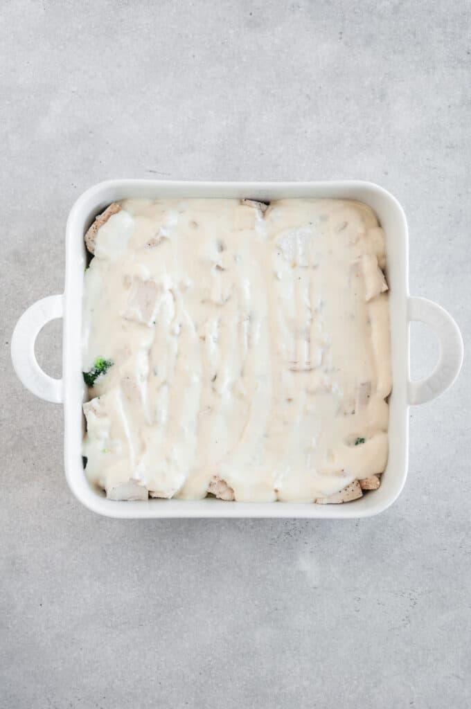 Creamy sauce layered in casserole dish for chicken divan.