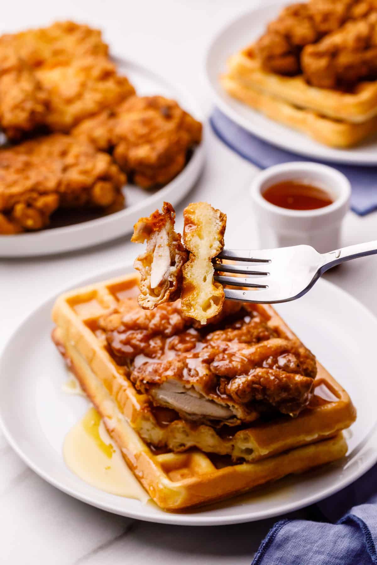 chicken and waffles with syrup served on a white round plate with a forkful of chicken and waffles 