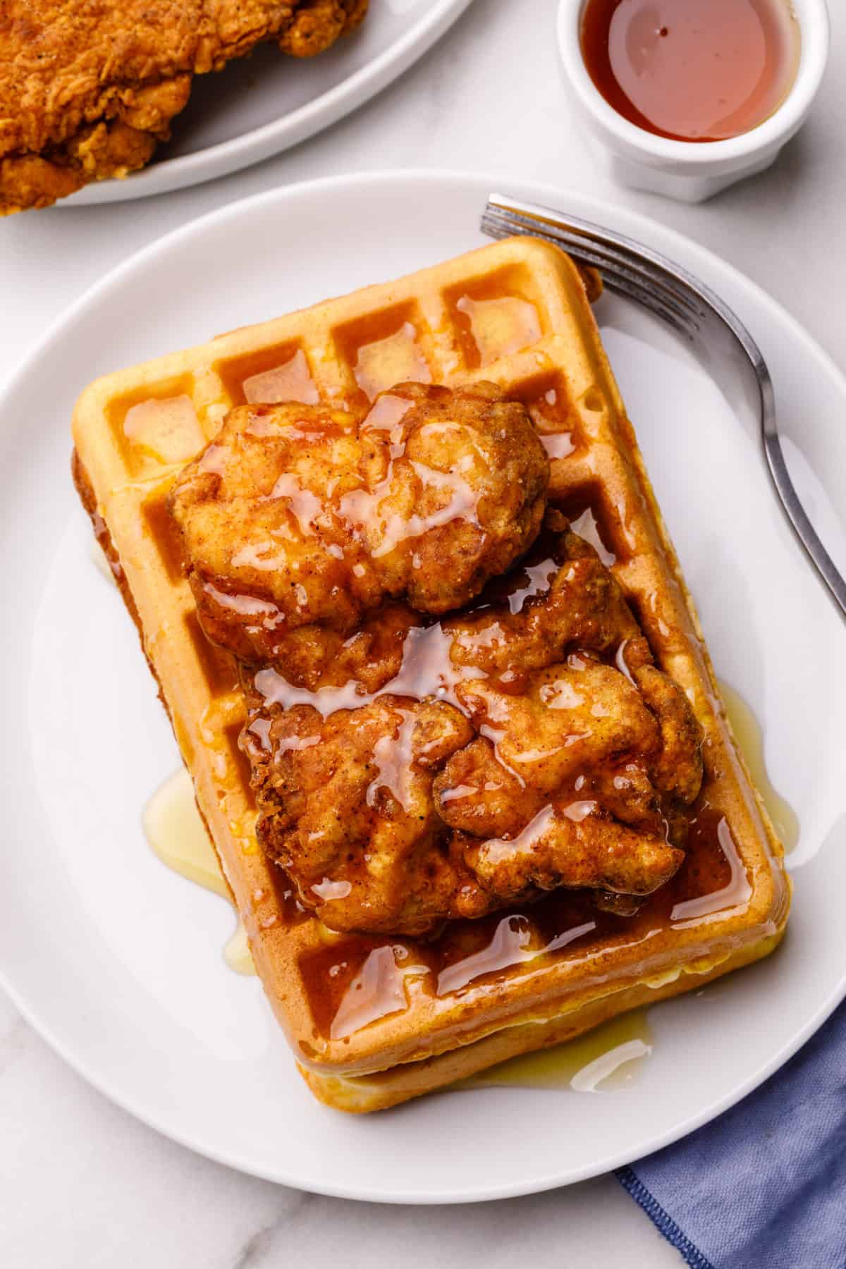 top down view of chicken and waffles with syrup served on a white round plate with a silver fork