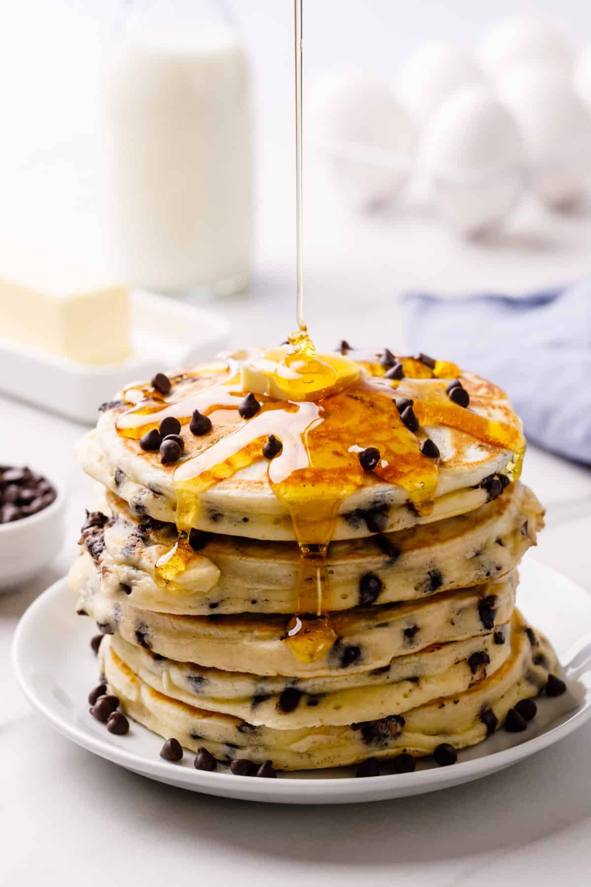 stack of chocolate chip pancakes topped with a slab of butter, syrup, and chocolate chips served on a white plate