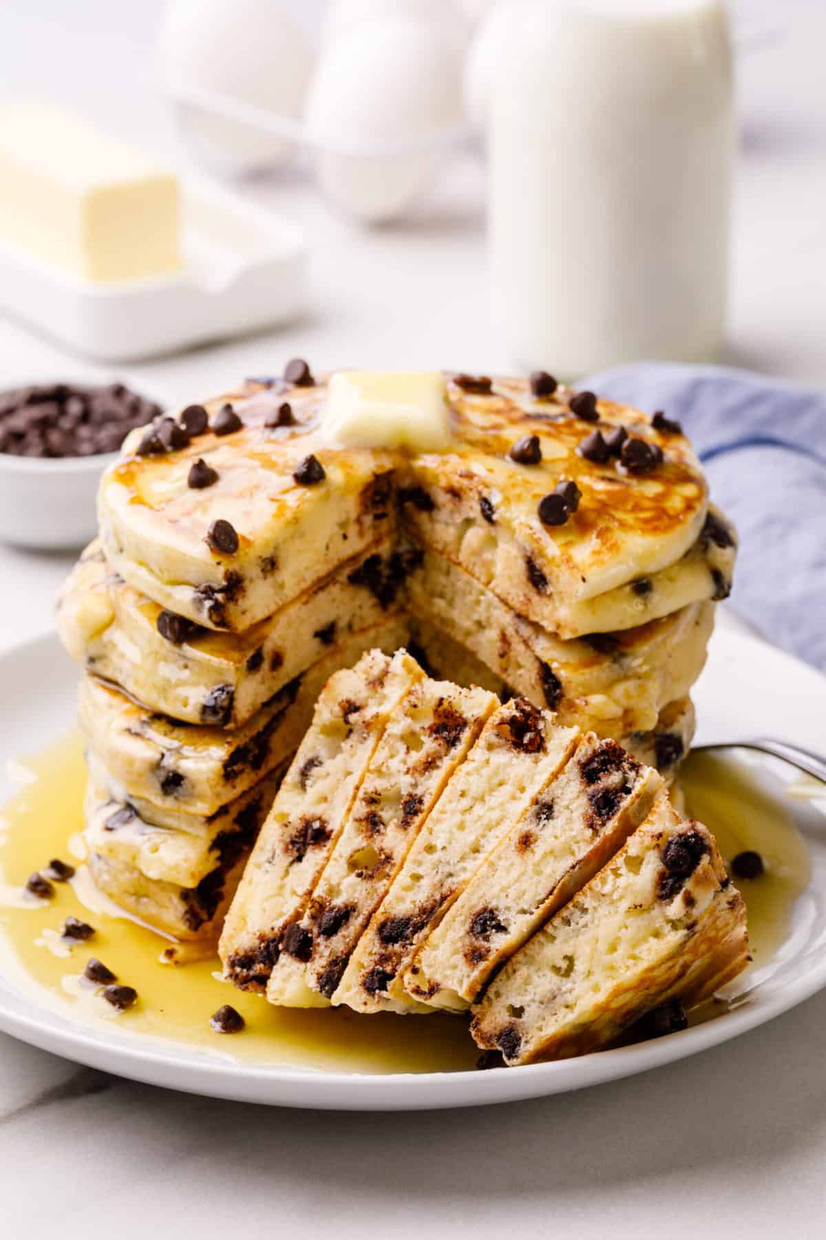 stack of chocolate chip pancakes with syrup served on a plate, pancakes are cut into to show the cross section