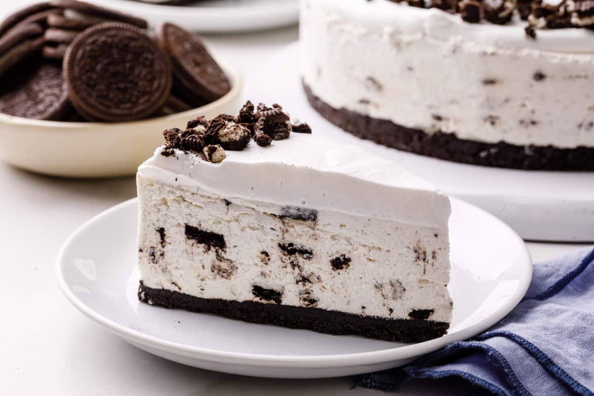A slice of Oreo no-bake cheesecake next to a bowl of Oreos and the rest of the cake. 