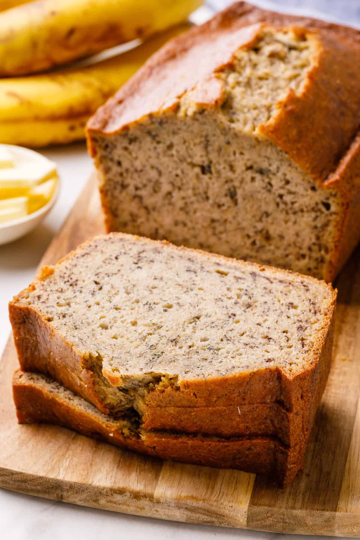 sour cream banana bread sliced on a wooden board with three slices of banana bread stacked on one another