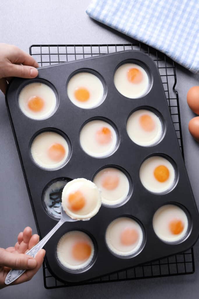 Woman holding spoon with baked egg over muffin tin