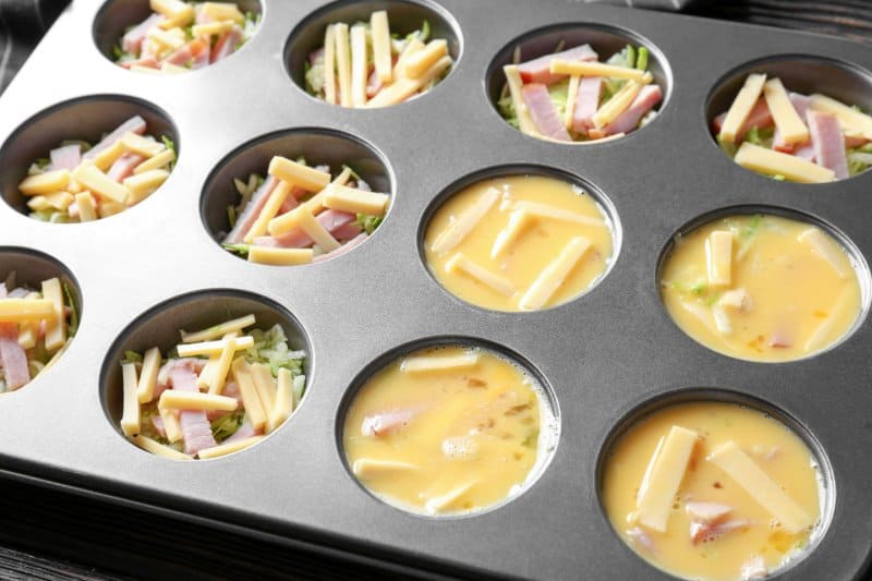 Whipped eggs, sliced cheese and ham in baking mold, closeup