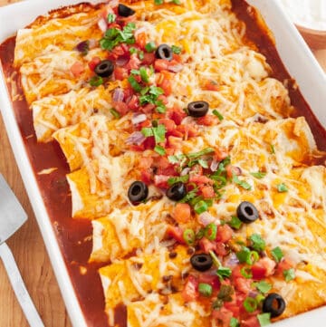 A baking dish full of beef enchiladas with red sauce.