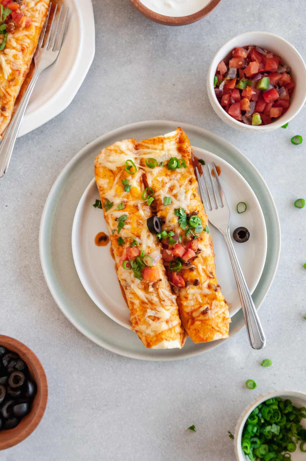 two beef enchiladas served on a stack of two plates with a silver fork.