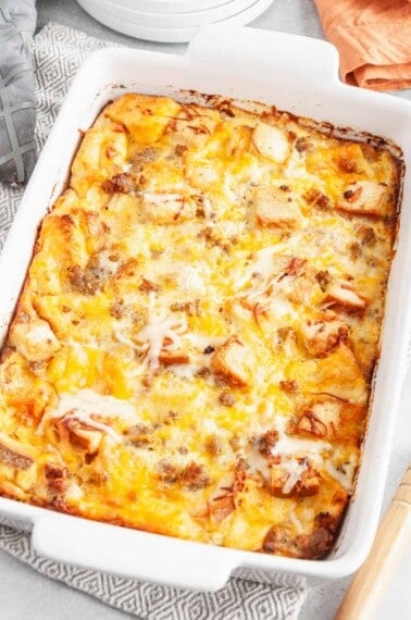 A baking dish full of cheesy sausage and egg casserole with bread.