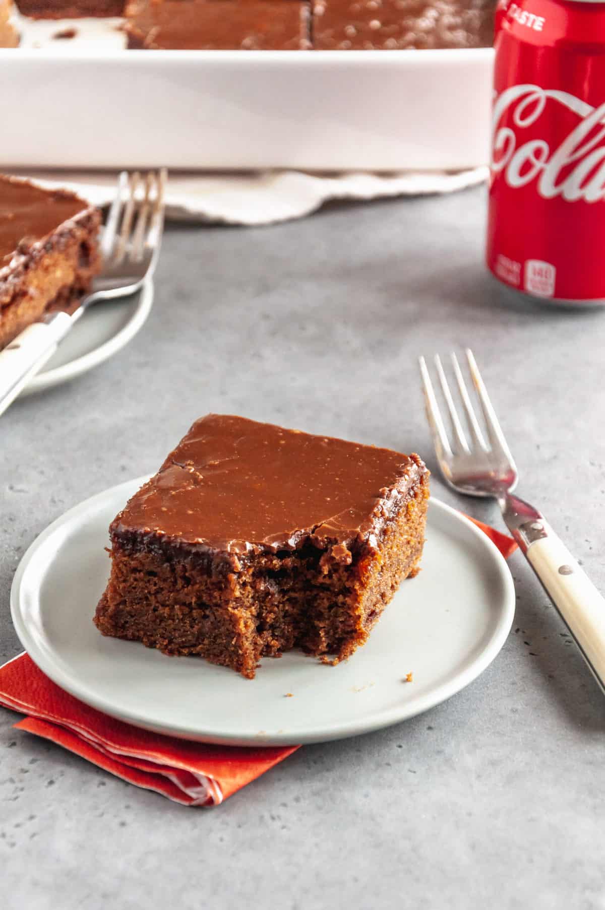 slice of coca cola cake with a bite taken out of it served on a round plate with a fork