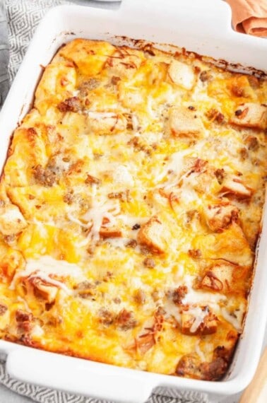 A baking dish full of cheesy sausage and egg casserole with bread.