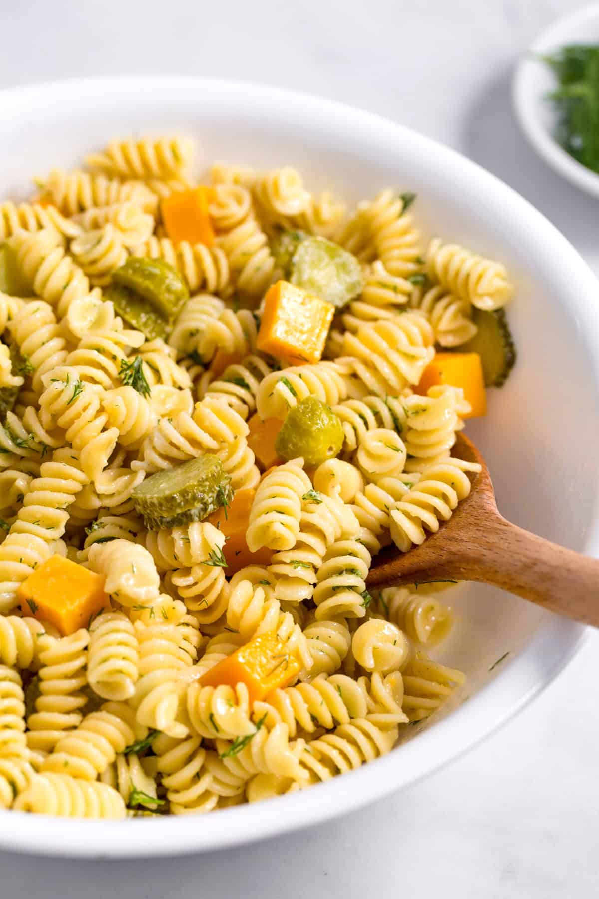 close up of dill pickle pasta salad with a wooden spoon