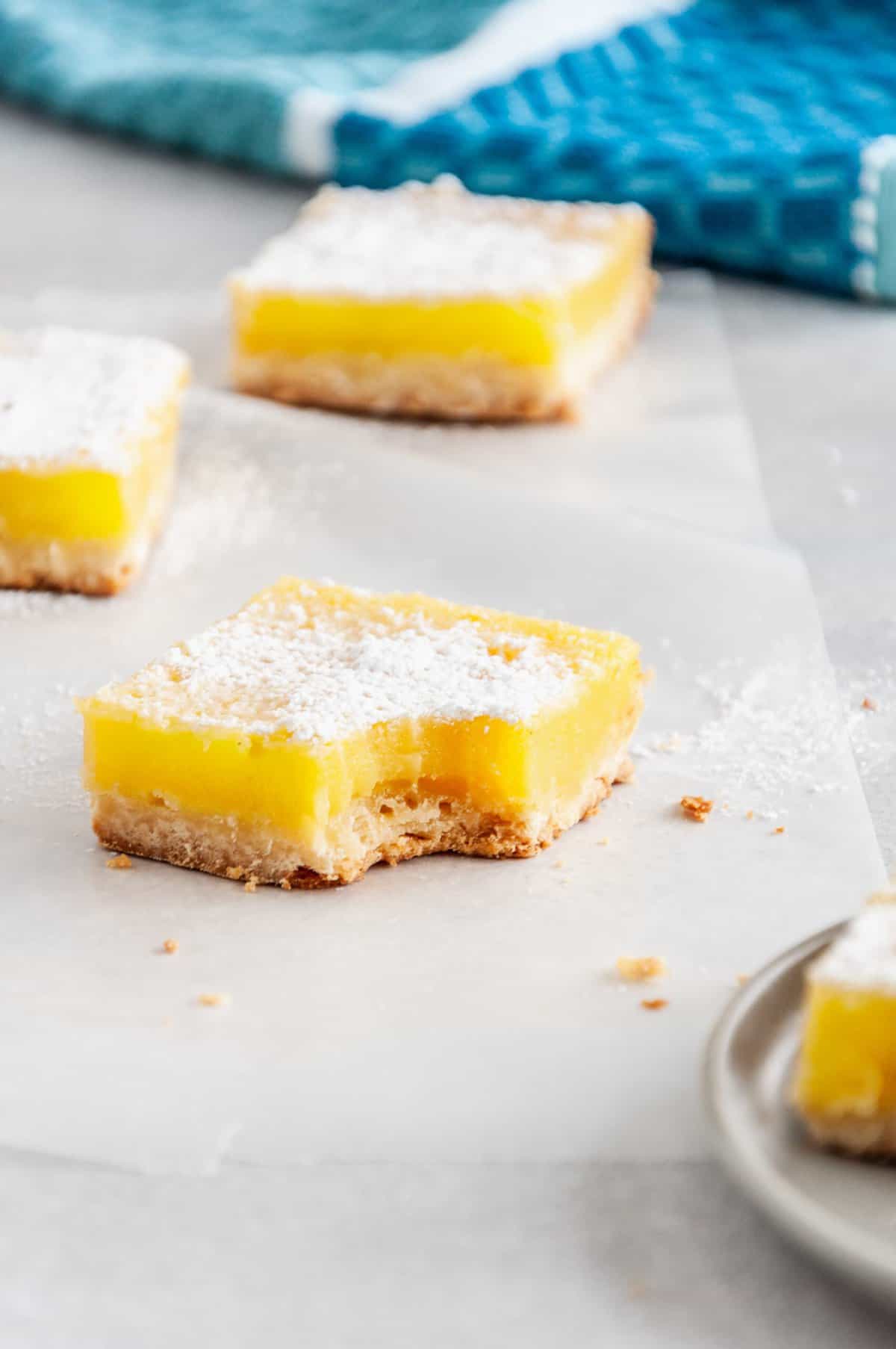square lemon bar with a bite taken out of it sitting on parchment baking paper