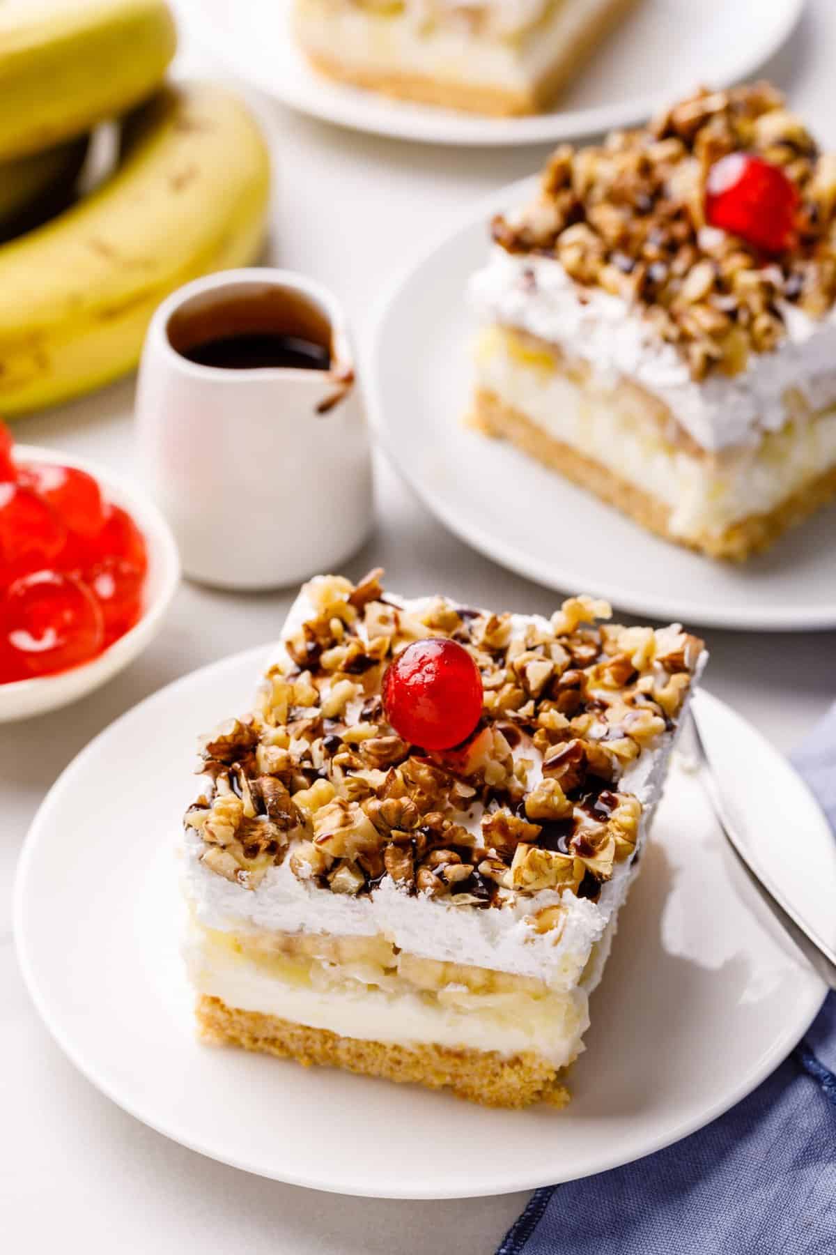 square slice serving of banana split cake served on a white round plate with a silver fork