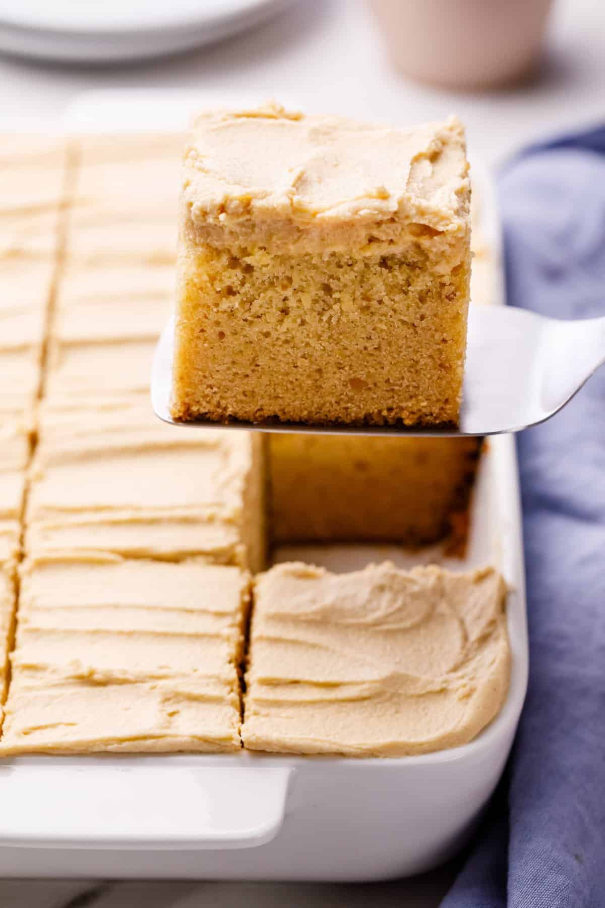 slices of peanut butter cake in a baking dish with one serving sitting on a metal cake spatula