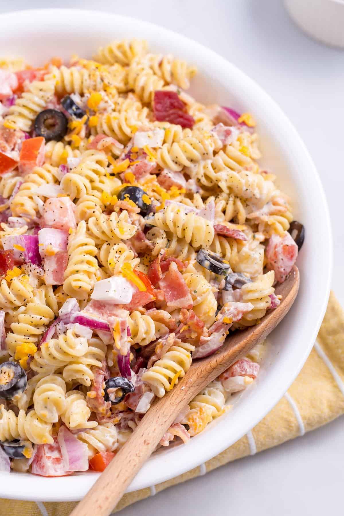 close up image of a bowl of bacon ranch pasta salad with a wooden spoon