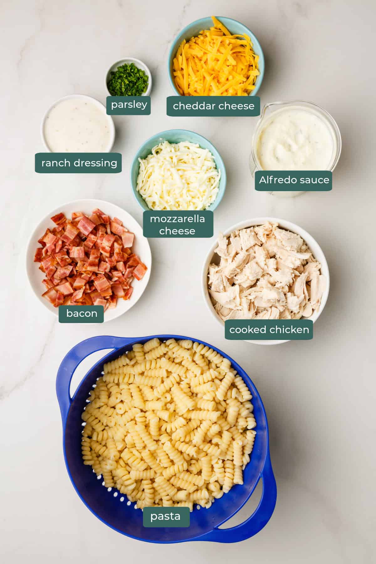 All of the ingredients for chicken bacon ranch in bowls on a white countertop.