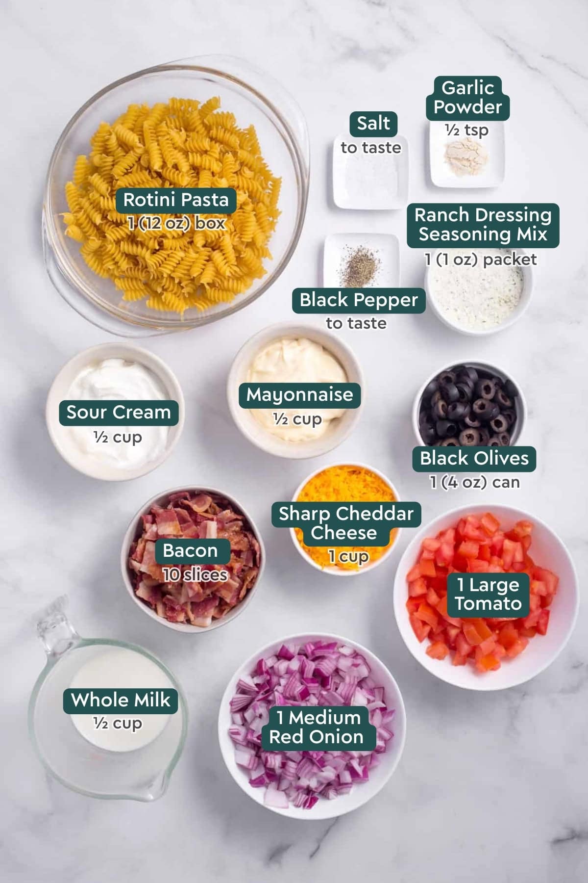 Ingredients for bacon ranch pasta salad, including rotini, seasonings, ranch, mayo, sour cream, olives, cheese, tomatoes, bacon, milk, red onion.