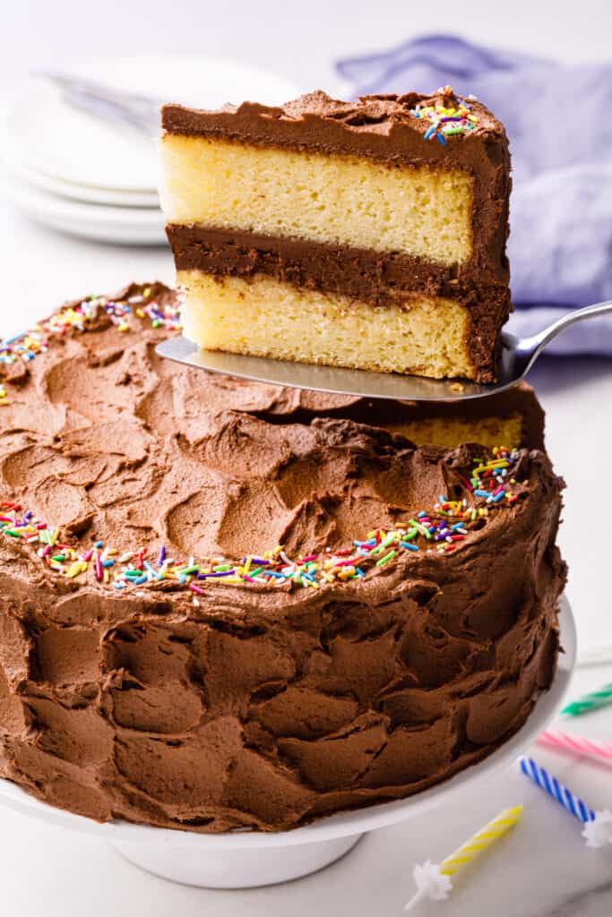 A yellow cake with chocolate frosting with a slice being lifted up.