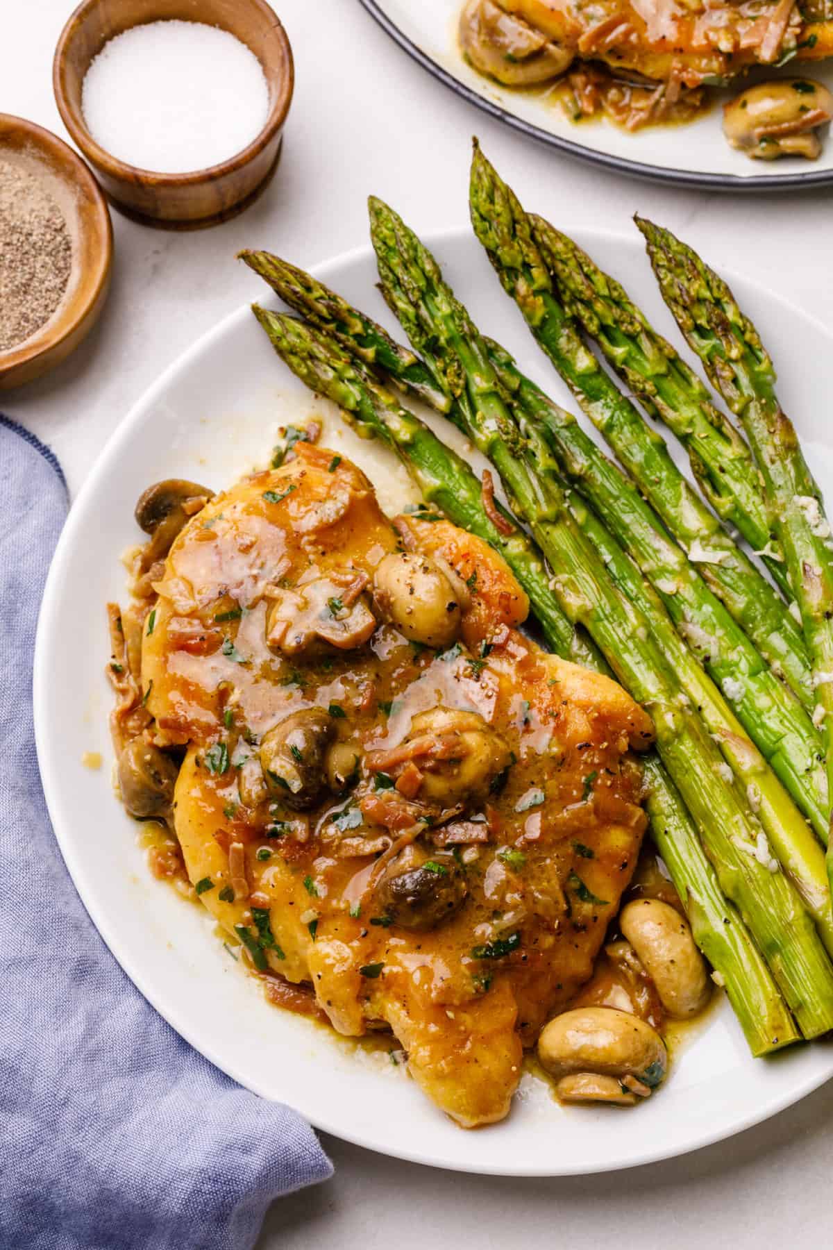 chicken marsala served on a white plate with a side of roasted asparagus