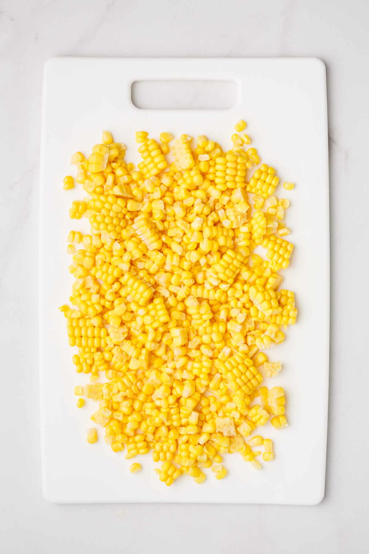 Corn kernels on a white cutting board. 