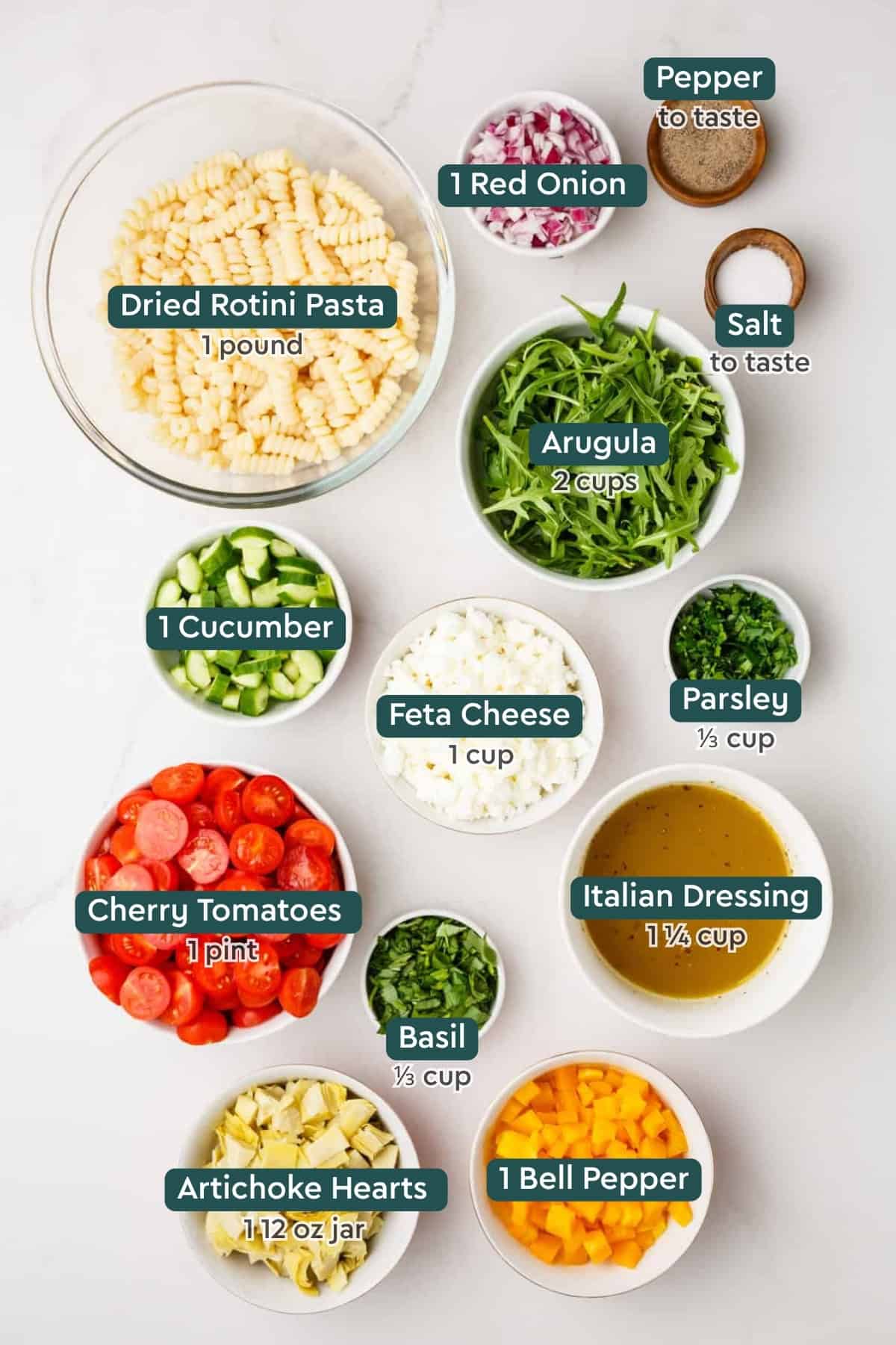 Ingredients for summer pasta salad, including rotini, arugula, onion, salt, pepper, cucumber, feta, parsley, tomatoes, basil, dressing, bell pepper, artichoke.
