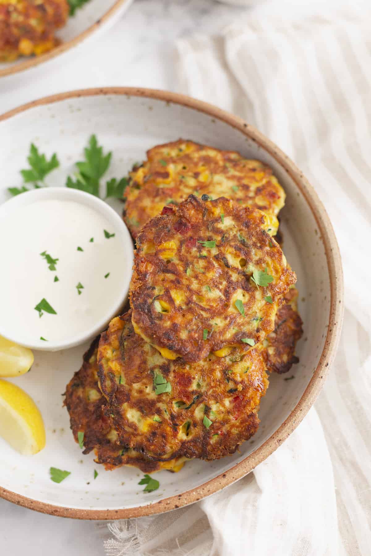 close up image of zucchini corn fritters with a side dipping sauce and lemon wedges served on a plate