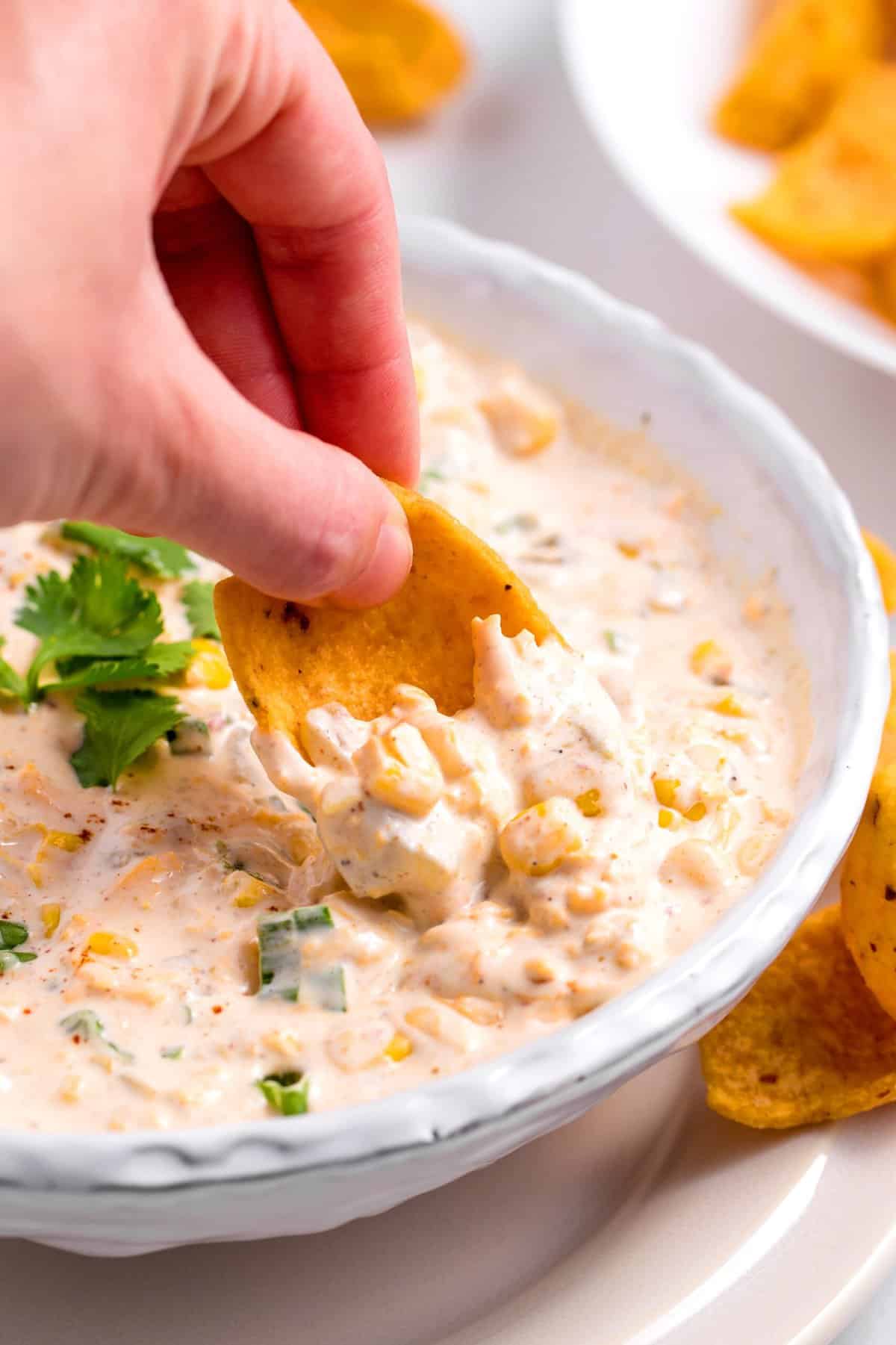 corn scoop chip dipping into homemade corn dip that is served in a bowl topped with cilantro