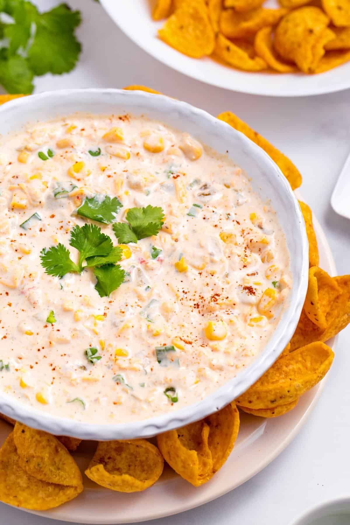 corn dip served in a white round bowl with a side of scoop shape corn tortilla chips