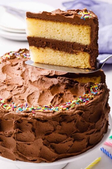 A yellow cake with chocolate frosting with a slice being lifted up.