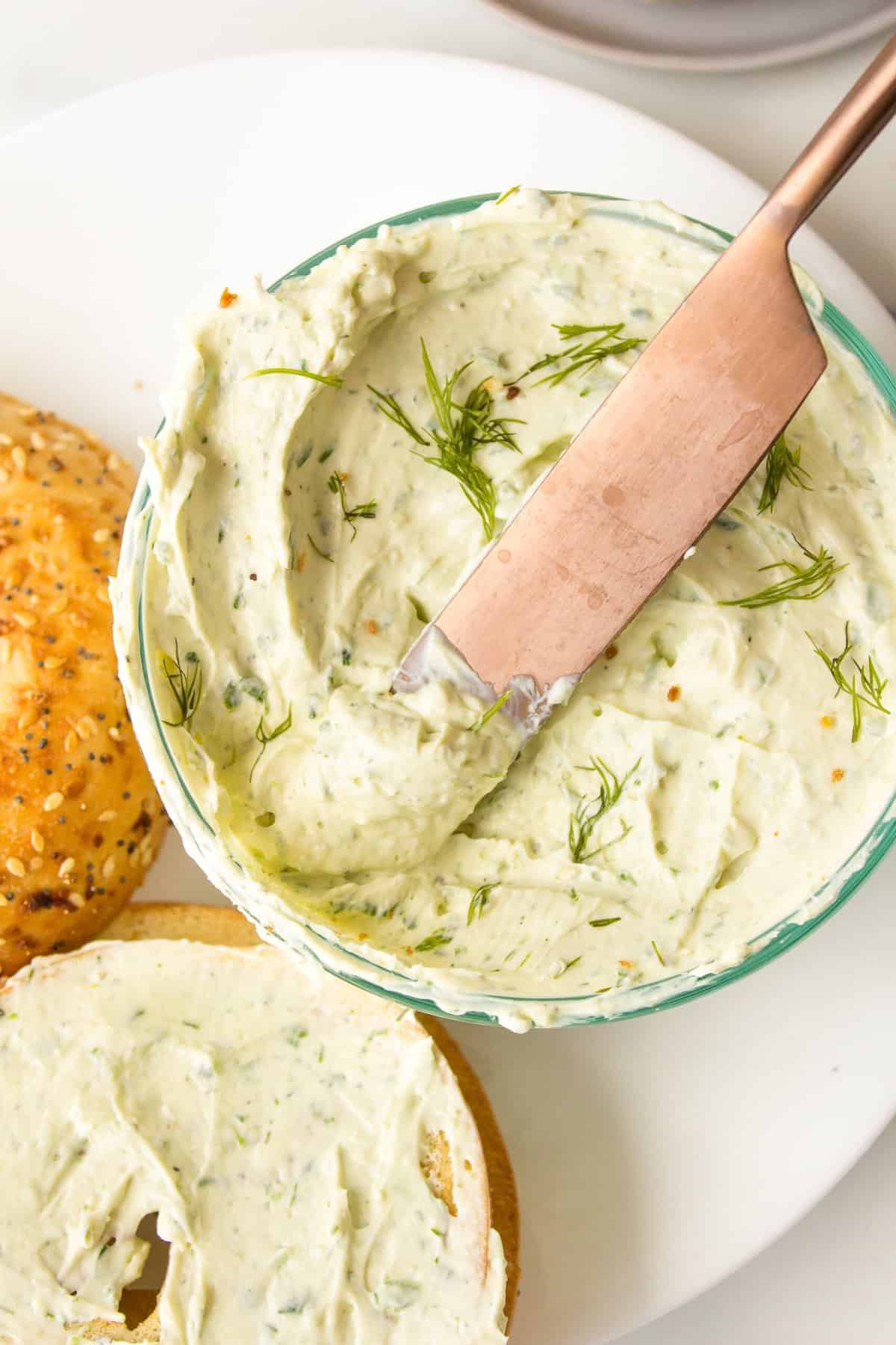 herb cream cheese dup served in a glass bowl with a gold butter knife