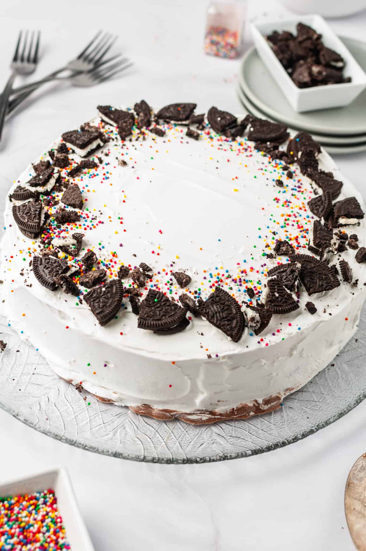 Copycat Dairy Queen Ice Cream Cake topped with crushed Oreos and sprinkles served on a glass cake plate.