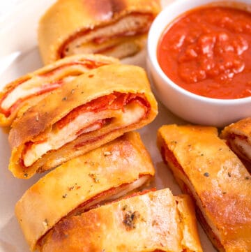 Pepperoni bread pieces on a plate with a bowl of marinara.