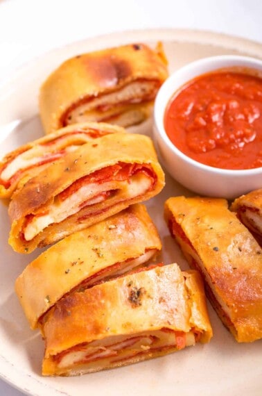 Pepperoni bread pieces on a plate with a bowl of marinara.
