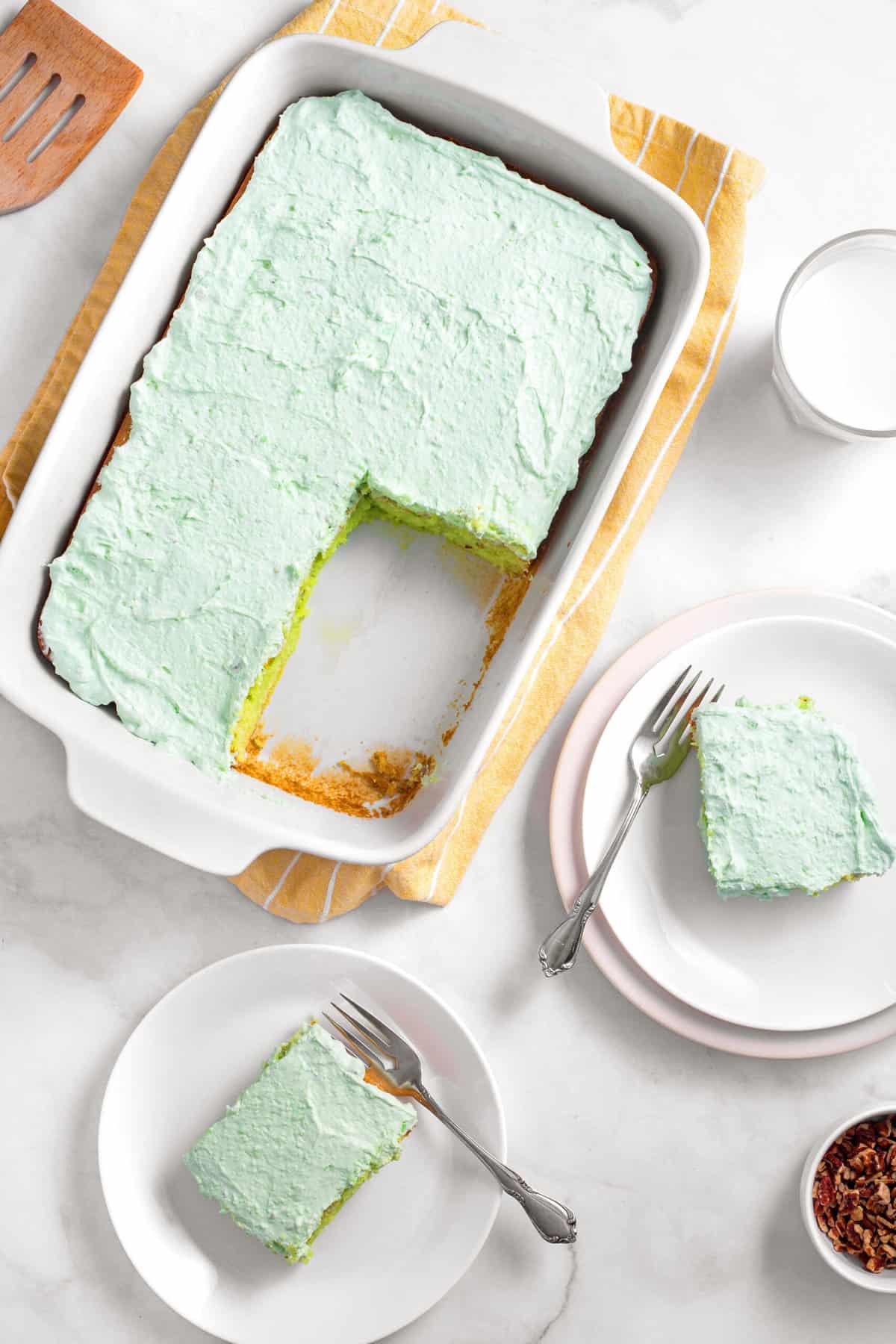 top down image of pistachio cake served in a casserole baking dish with two servings of pistachio cake on plates