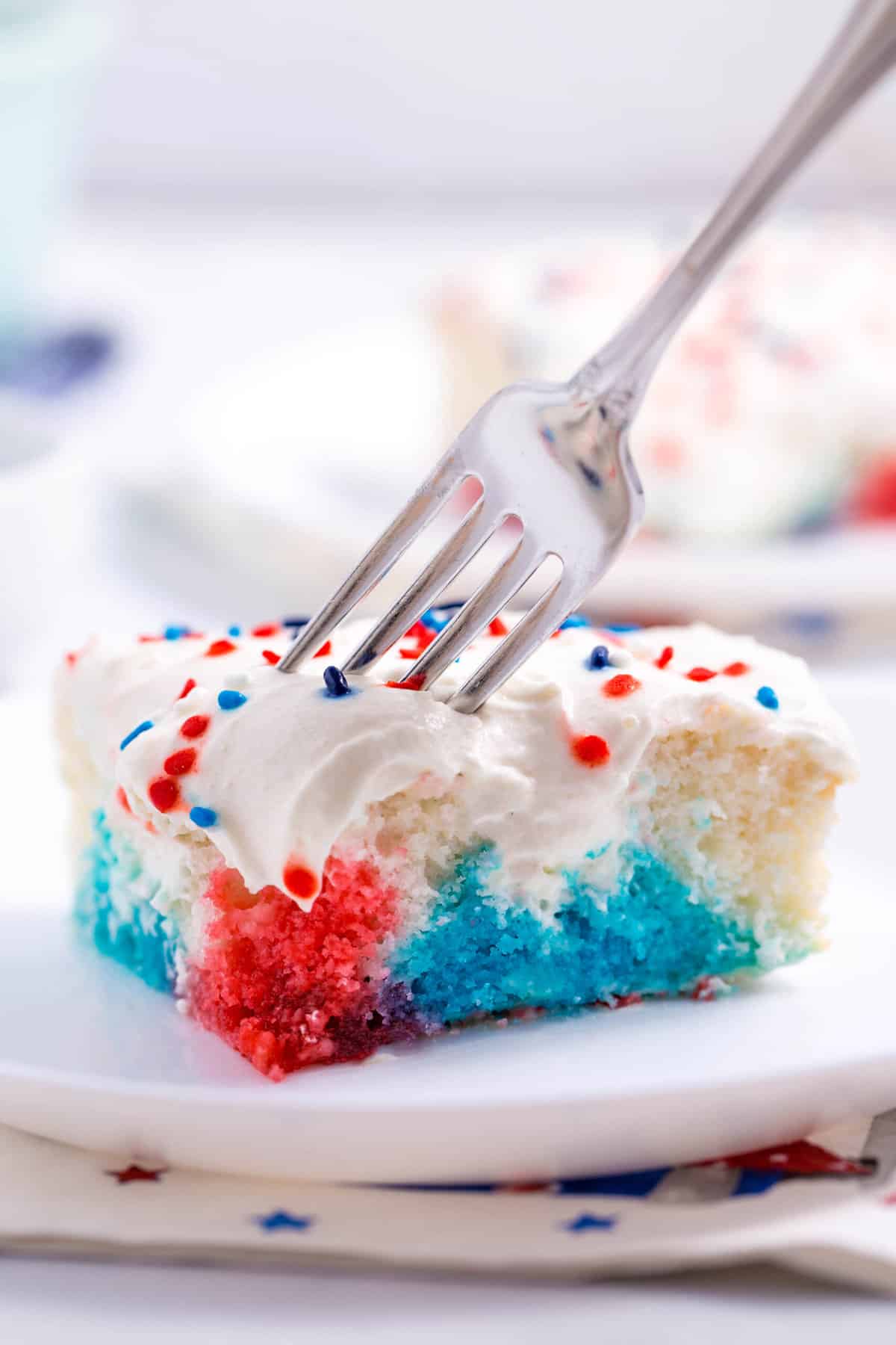 fork digging into a serving of red, white, and blue poke cake served on a white round plate