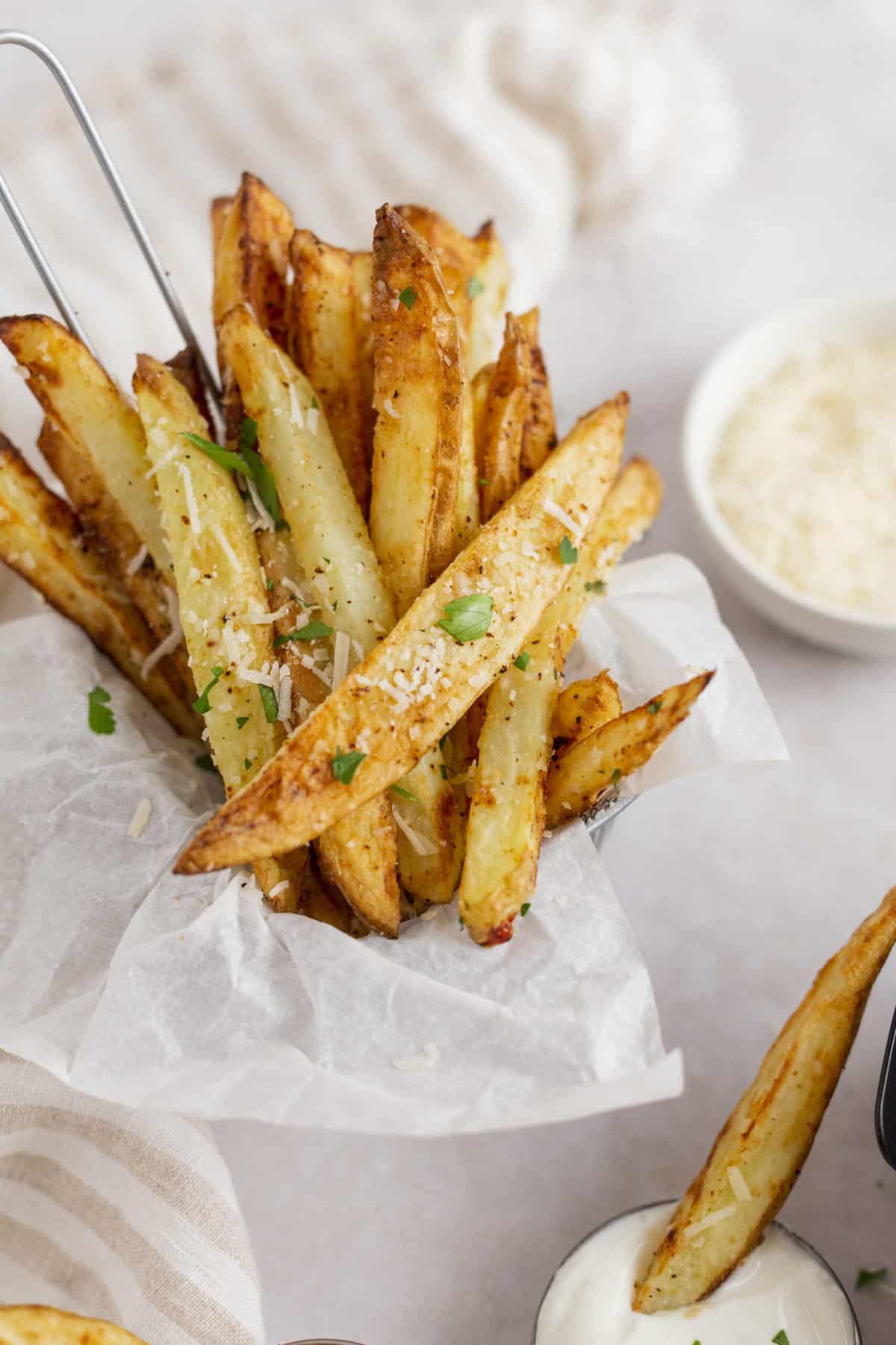 air fryer parmesan fries served in a parchment lined cup with one fry dipping into ranch