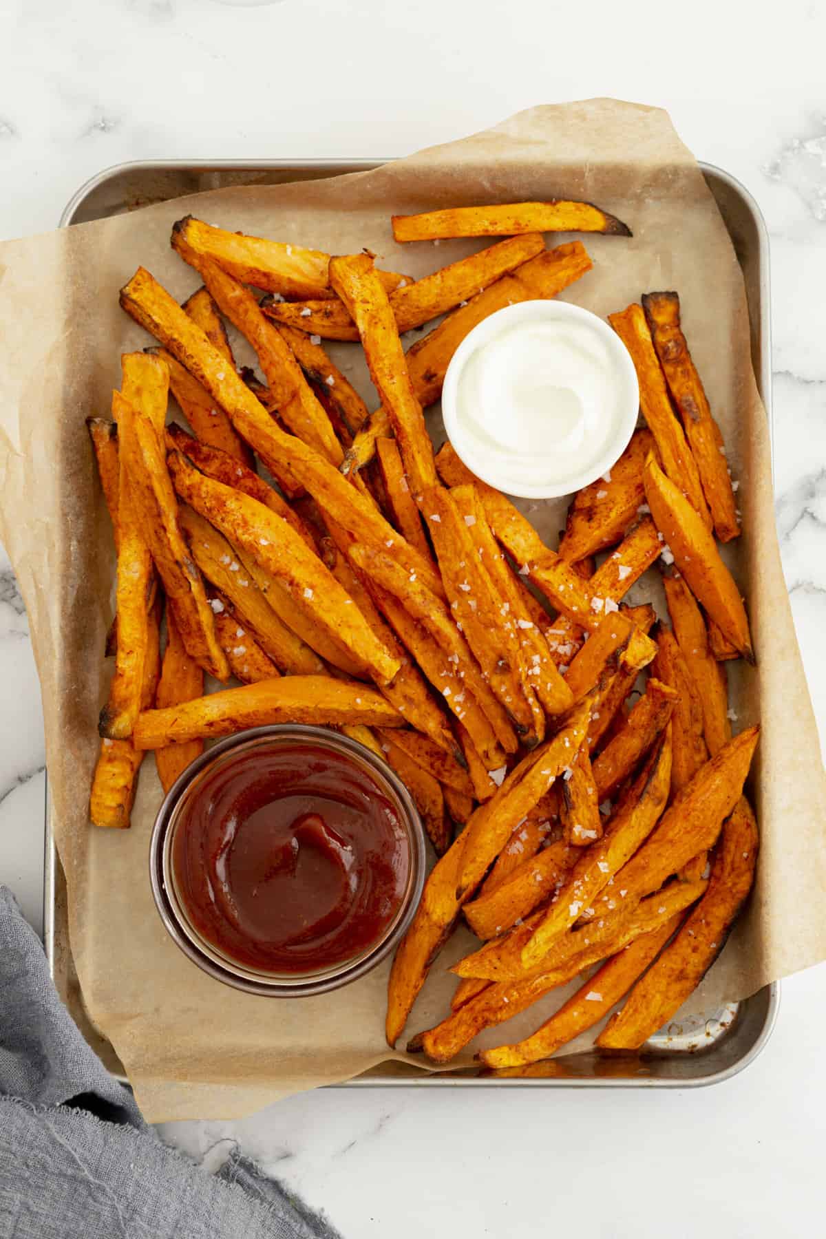 top down image of air fryer sweet potato fries served on a baking sheet lined with parchment paper and sides of ranch and ketchup in small side dish bowls
