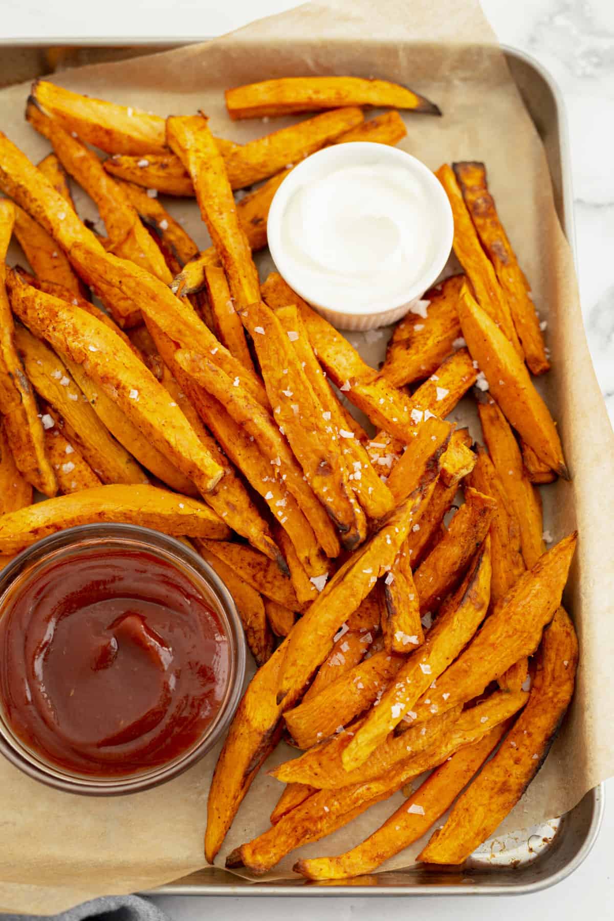 top down view of air fryer sweet potato fries served on a baking sheet with a side of ketchup and ranch