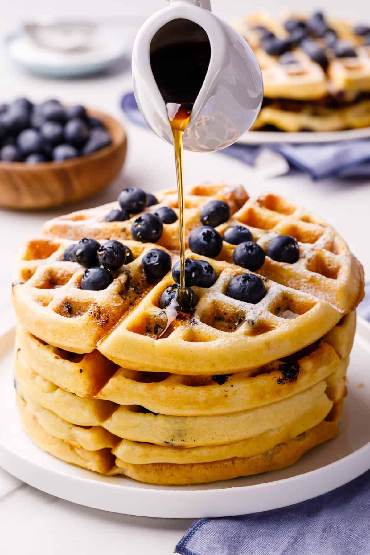 syrup being poured on a stack of homemade blueberry waffles