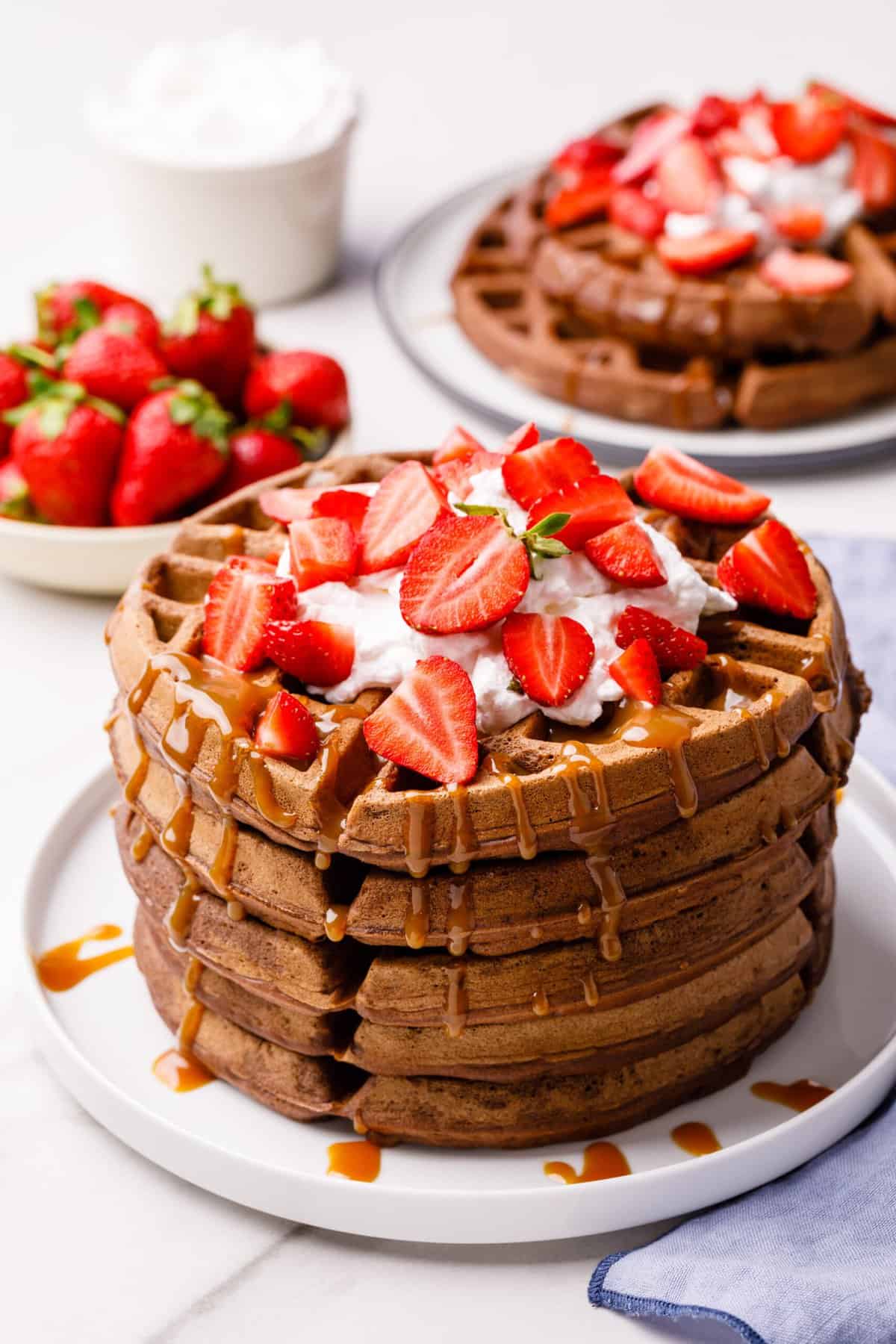 stack of chocolate waffles with whipped cream and fresh strawberries topped with caramel sauce
