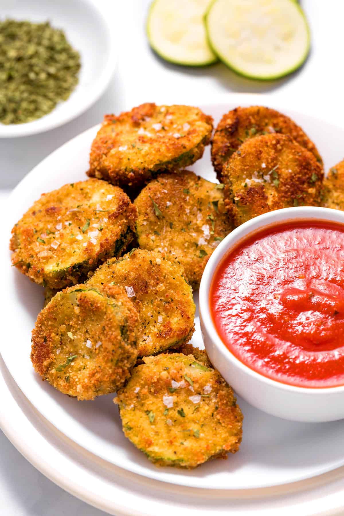 close up image of zucchini fries with a side of marinara sauce served on a white round plate