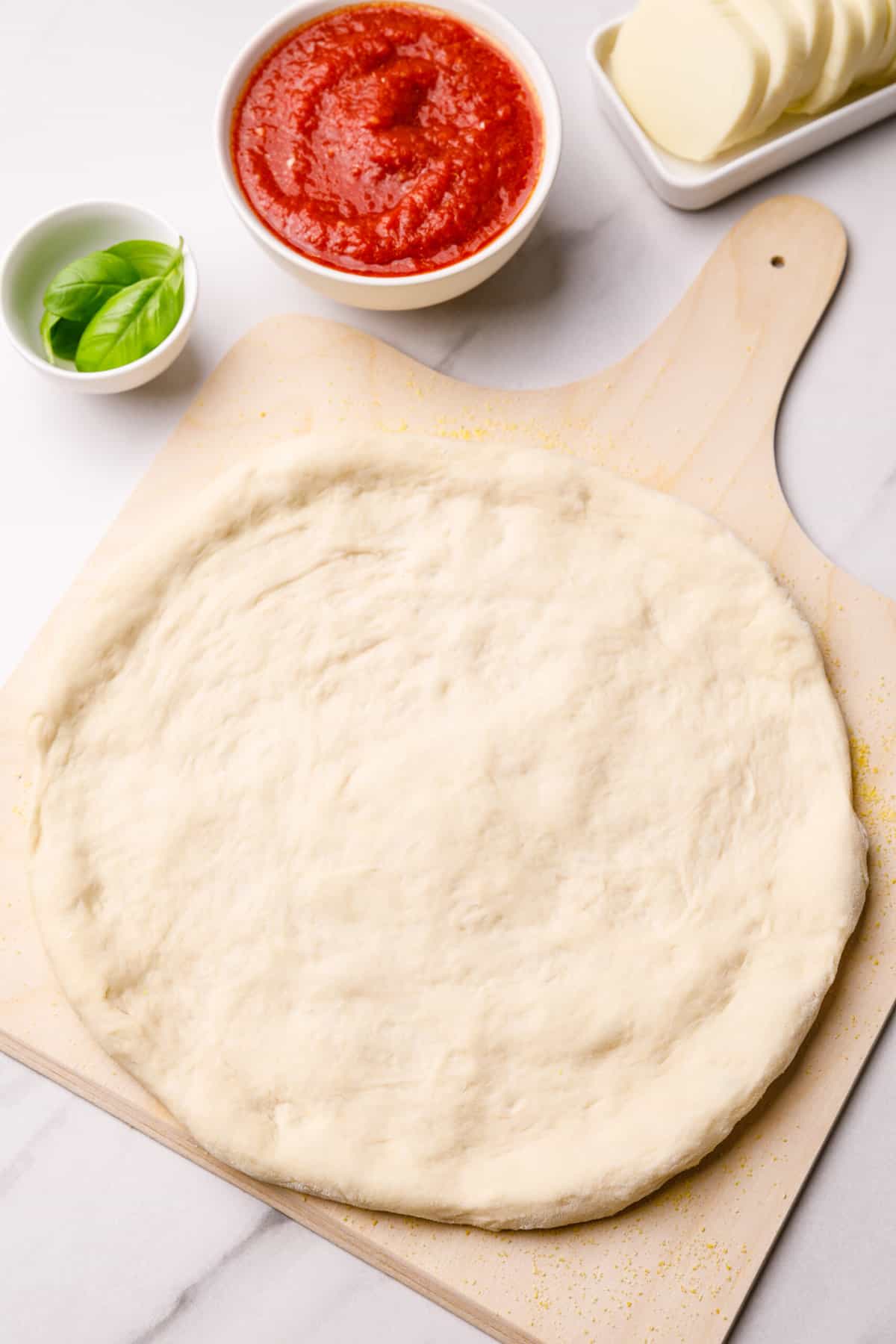 formed pizza dough in a shape of a crust sitting on wooden pizza platter