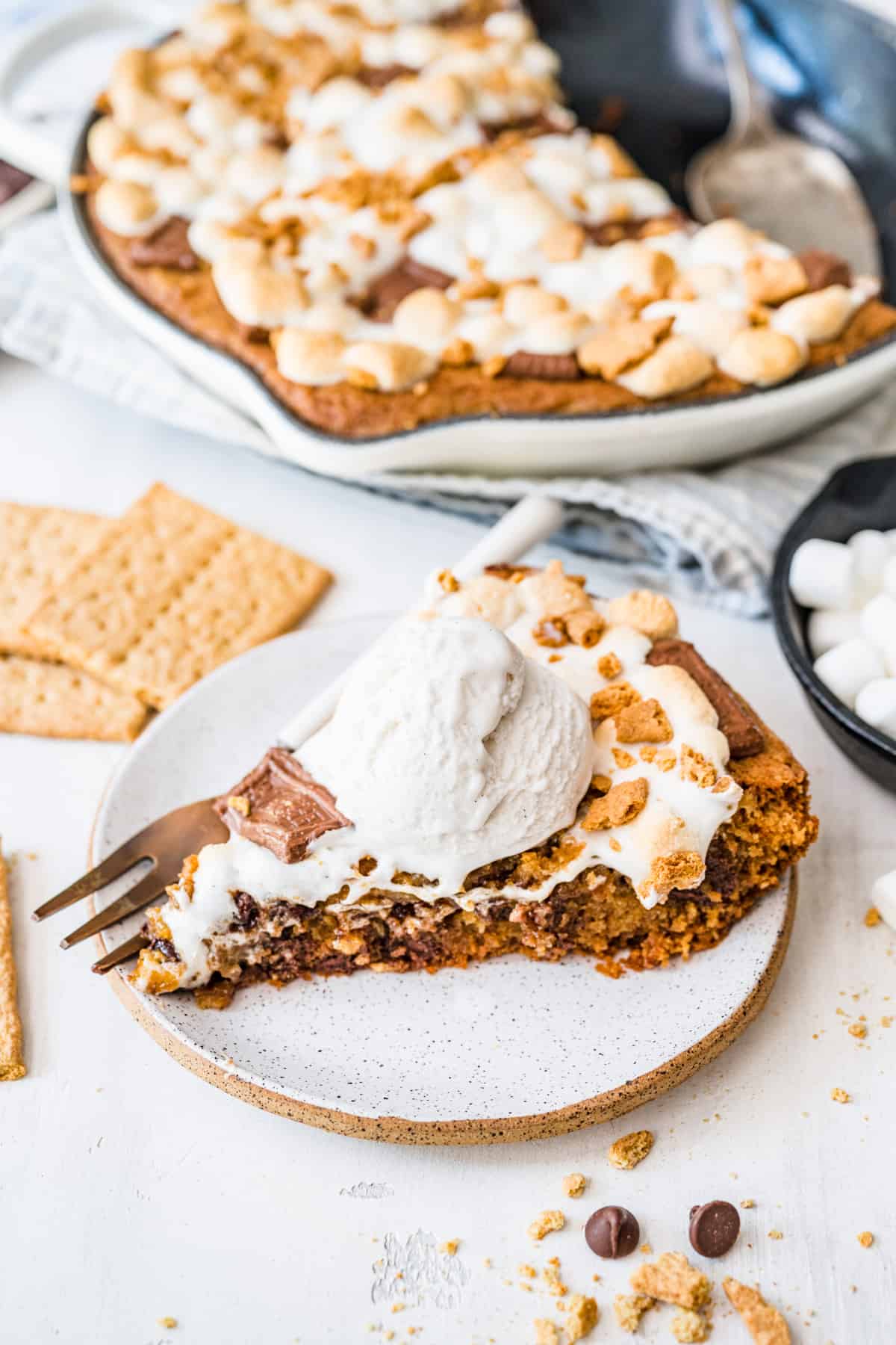 slice of smores cookie skillet served on a plate with a fork and topped with a scoop of vanilla bean ice cream