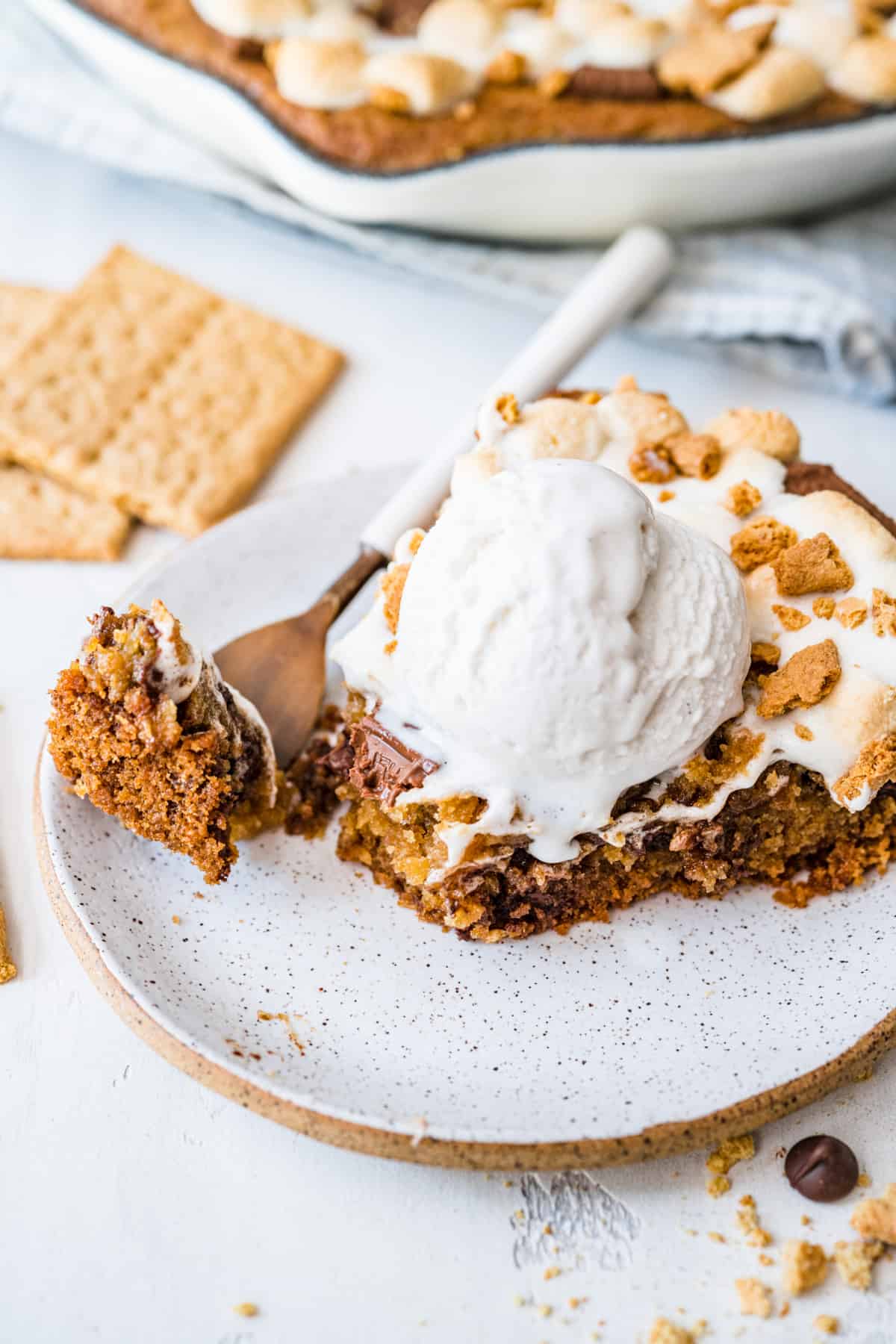 serving of cookie smores skillet with a scoop of vanilla bean ice cream on top and a forkful of cookie served on a plate